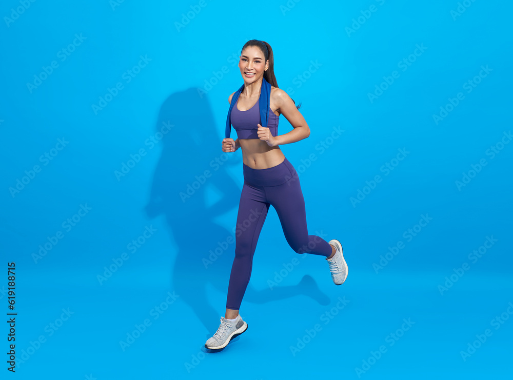 Happy young Asian active woman running and jumping isolated in studio on blue color background. Isolated healthy women in sportswear workout sprinting.