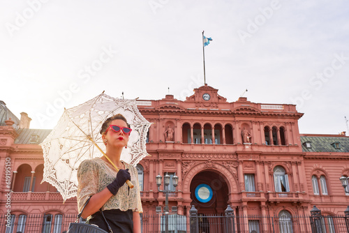caucasian actrees woman dressed in vintage clothes and umbrella in the street with The Casa Rosada in the background © oscargutzo
