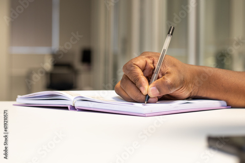 Close up of a black man writing in notebook in an office