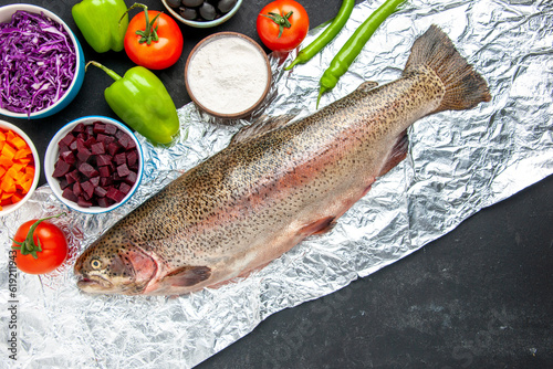 Above view of scales removed fresh fish chopped vegetables flour in a bowl on dark color background photo