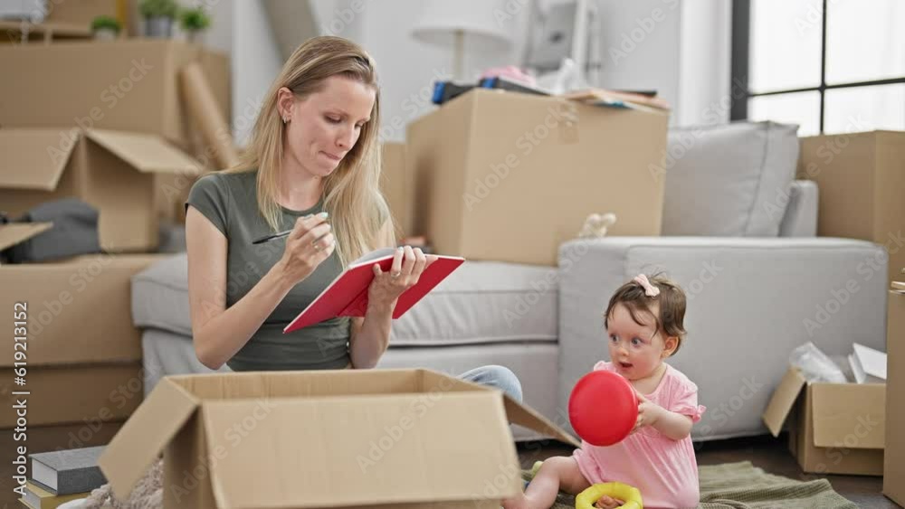 Mother and daughter writing on notebook checking playing on floor at new home Mother and daughter writing on notebook checking playing on floor at new home