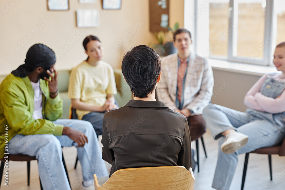 Rear view of specialist sitting on chair and talking to young people during psychotherapy in office