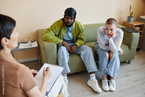 Young multiethnic couple talking to psychologist during their meeting in office
