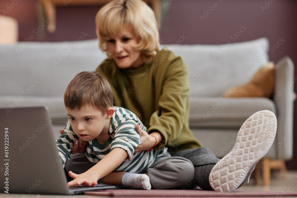 Portrait of little boy with down syndrome using laptop at home with caring mother assisting Portrait of little boy with down syndrome using laptop at home with caring mother assisting