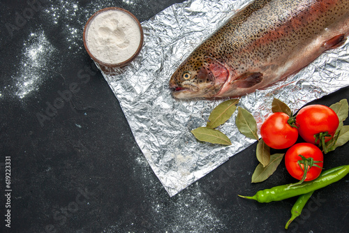 Horizontal view of scales removed fresh fish vegetables flour in a bowl on dark color background photo