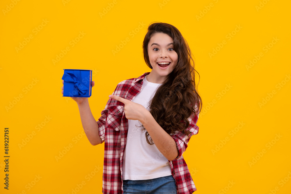 Happy teenager, positive and smiling emotions of child girl. Teenager kid with present box on isolated yellow background. Teen girl giving birthday gift. Present, greeting and gifting concept. Happy teenager, positive and smiling emotions of child girl. Teenager kid with present box on isolated yellow background. Teen girl giving birthday gift. Present, greeting and gifting concept.
