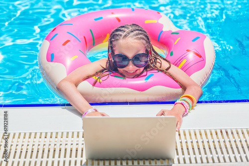 Young girl with sunglasses in inflatable circle in swimming pool using her laptop computer.