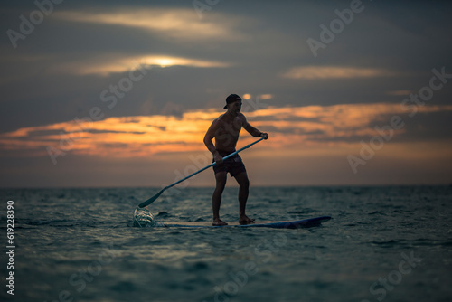 Active male surfer balancing on standup paddleboard in sea