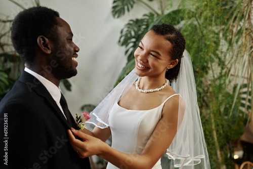 Waist up portrait of smiling black woman as beautiful bride meeting groom before wedding ceremony indoors photo