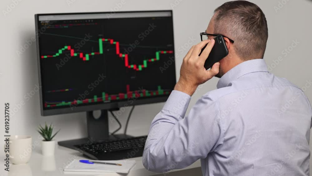 Close-up view of the trader who is monitoring invest analytics on the monitor screen and talking on the phone Close-up view of the trader who is monitoring invest analytics on the monitor screen and talking on the phone