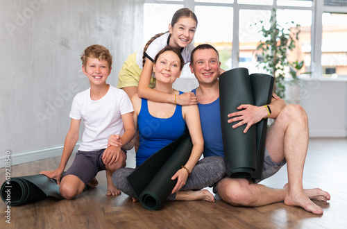 Happy family members sitting on the floor with black mats in hands in training room © JackF