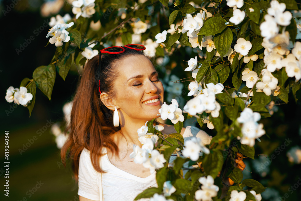 smiling trendy woman in white shirt near flowering tree smiling trendy woman in white shirt near flowering tree