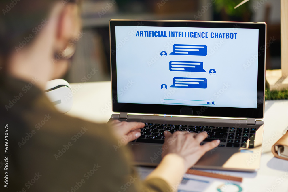 Seen from behind modern woman with laptop having robot chat Seen from behind modern woman with laptop having robot chat