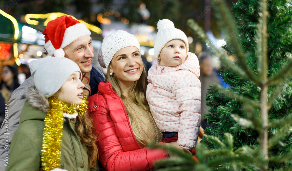 Portrait of smiling man and his happy wife and daughters buying tree at Christmas market