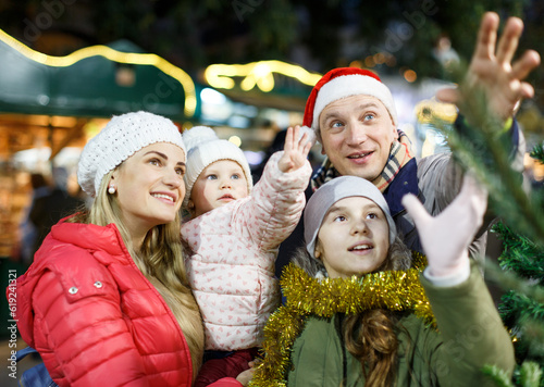 Portrait of smiling man and his happy wife and daughters buying tree at Christmas market