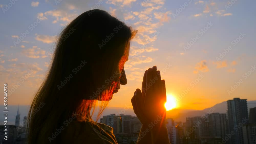 Young woman silhouette is folding hands and praying against the sunrise ...
