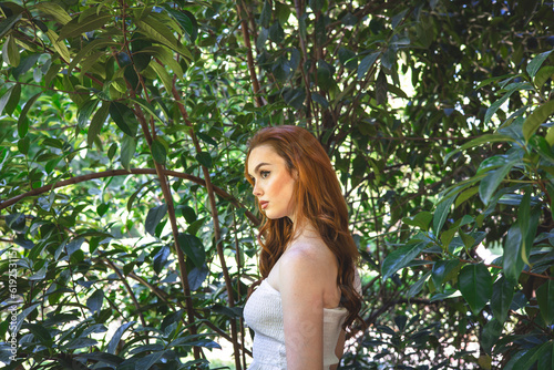 very beautiful freckled white woman with long red hair in a garden of green leaves