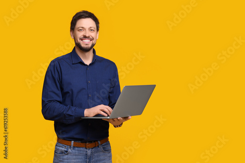 Happy man with laptop on yellow background, space for text