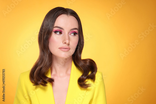 Portrait of beautiful young woman with makeup and gorgeous hair styling on yellow background. Space for text © New Africa