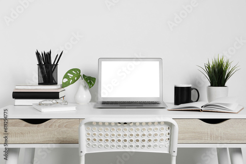 Cozy workspace with laptop, houseplants and stationery on wooden desk at home