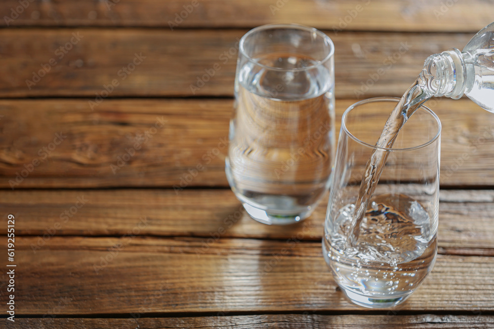 Pouring water from bottle into glass on wooden table, space for text Pouring water from bottle into glass on wooden table, space for text
