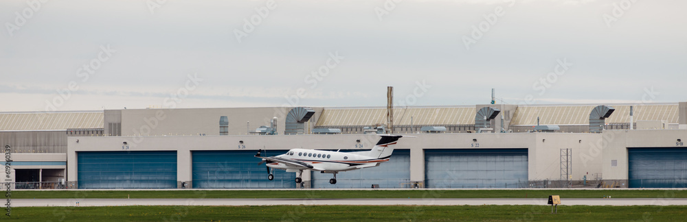 petit avion en train de décoller sur une piste de décollage d'un petit aéroport avec des portes de hangar bleu - obrazy, fototapety, plakaty 