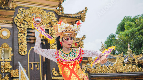 girl wearing Balinese traditional dress with a dancing gesture on Balinese temple background with hand-held fan, crown, jewelry, and gold ornament accessories. Balinese dancer woman portrait
 photo
