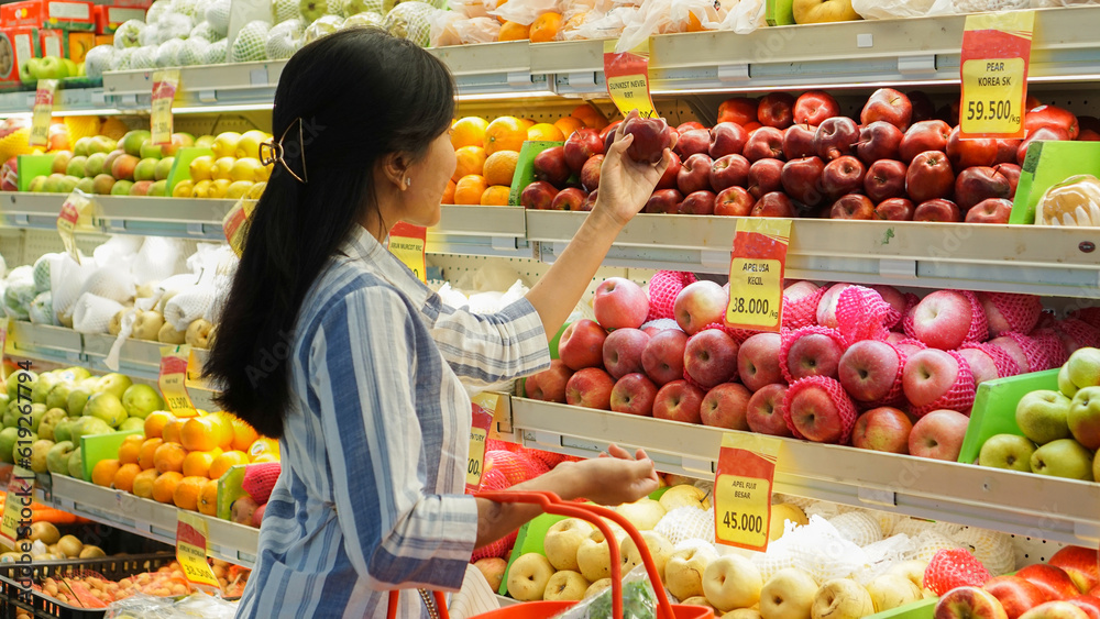 portrait of a beautiful Asian woman buying fruit arranged on a fruit rack in a supermarket 
