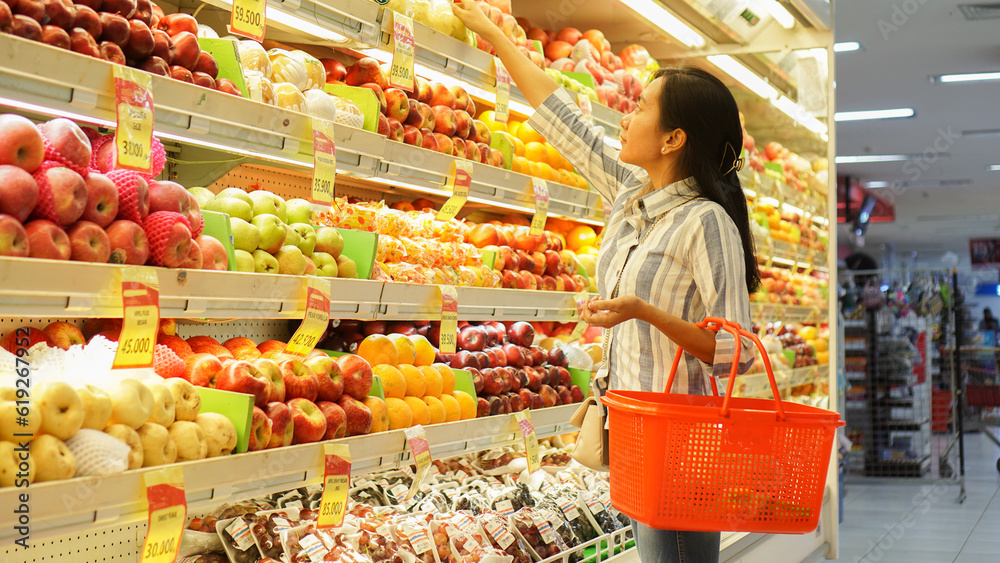 portrait of a beautiful Asian woman buying fruit arranged on a fruit rack in a supermarket 
