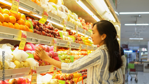 portrait of a beautiful Asian woman buying fruit arranged on a fruit rack in a supermarket 