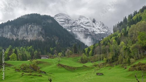 Timelapse, Serene Landscape of Swiss Alps, Green Meadows, Forest and Snow Capped Peaks in Moving Clouds photo