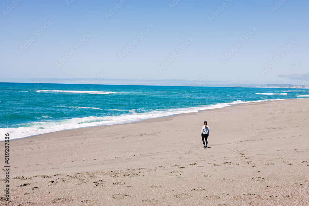 Woman standing on the empty ocean coast, view from the back