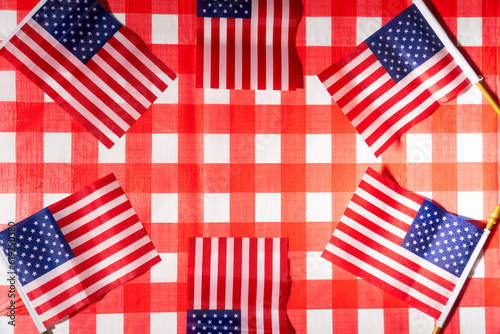 A top lay photo of a picnic table with a red and white checked tablecloth and little US flags forming a circle. The flags are arranged in a way that suggests patriotism and celebration.