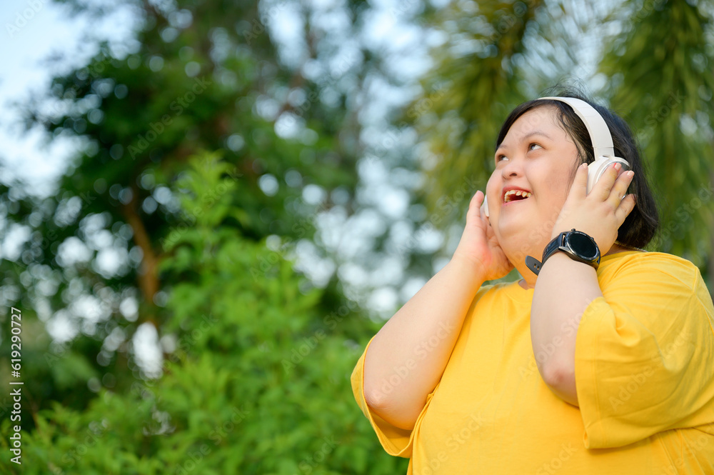 Asian girl with Down syndrome wearing headphones Smiling with happiness in the park in the middle of nature Asian girl with Down syndrome wearing headphones Smiling with happiness in the park in the middle of nature