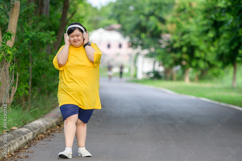 Asian girl with Down syndrome wearing headphones Smile and be happy by walking to burn fat and running slowly to exercise in a park in the middle of nature.
