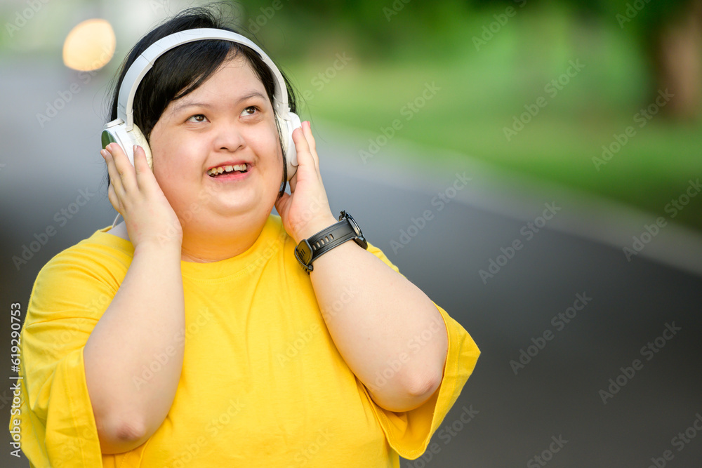 Asian girl with Down syndrome wearing headphones Smiling with happiness in the park in the middle of nature Asian girl with Down syndrome wearing headphones Smiling with happiness in the park in the middle of nature