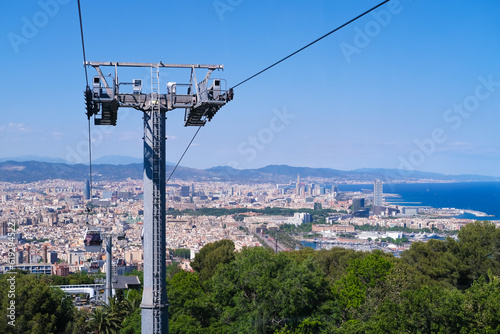 The funicular passes the support tower with a view from above of Barcelona and the sights. A trip by cable car to the observation decks. The funicular moves along the cable against the blue sky.
