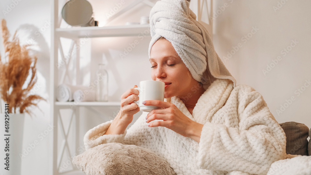 Morning coffee. Weekend relaxation. Spa leisure. Happy inspired woman in bathrobe with mug enjoying hot drink aroma on couch after bath at light home interior with free space. - obrazy, fototapety, plakaty 
