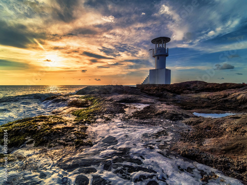 "Enchanting Coastal Serenity: Lighthouse, Rocks, and Evening Sun Overlooking the Sea Waves"