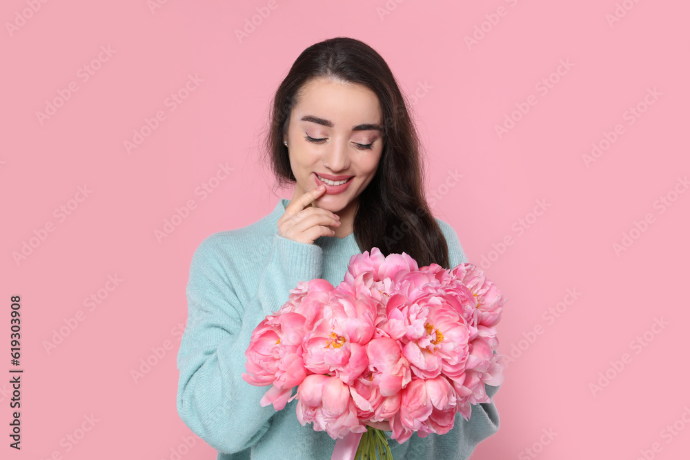 Beautiful young woman with bouquet of peonies on pink background