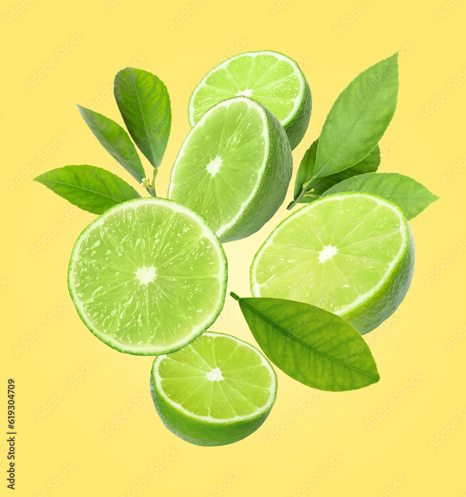 Fresh lime fruits and green leaves falling on yellow background
