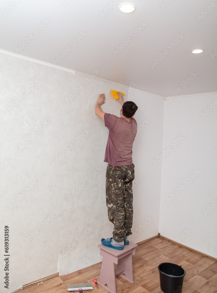 A worker pastes wallpaper on the walls in a room