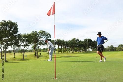 Golfers putting golf balls on the green amid the warm sunshine in the morning. Concept of Outdoor activities and Outdoor sports, Concept of Golfer and Lifestyle. 
