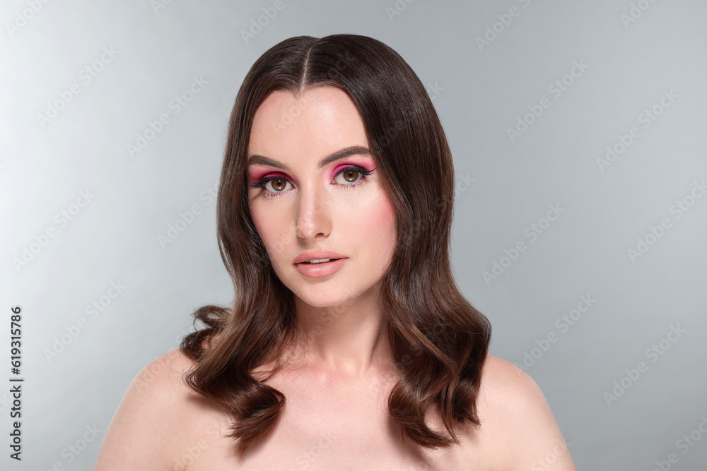 Portrait of beautiful young woman with makeup and gorgeous hair styling on light grey background