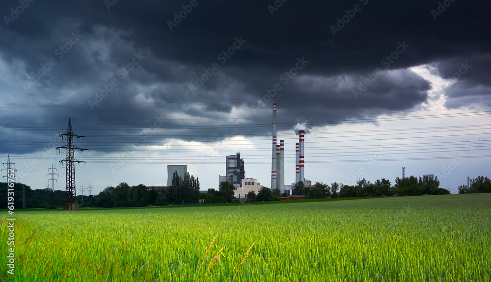 Dark clouds over a coal power plant under a green field of wheat