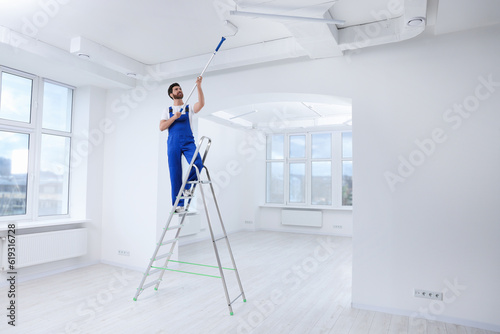 Handyman painting ceiling with roller on step ladder in room