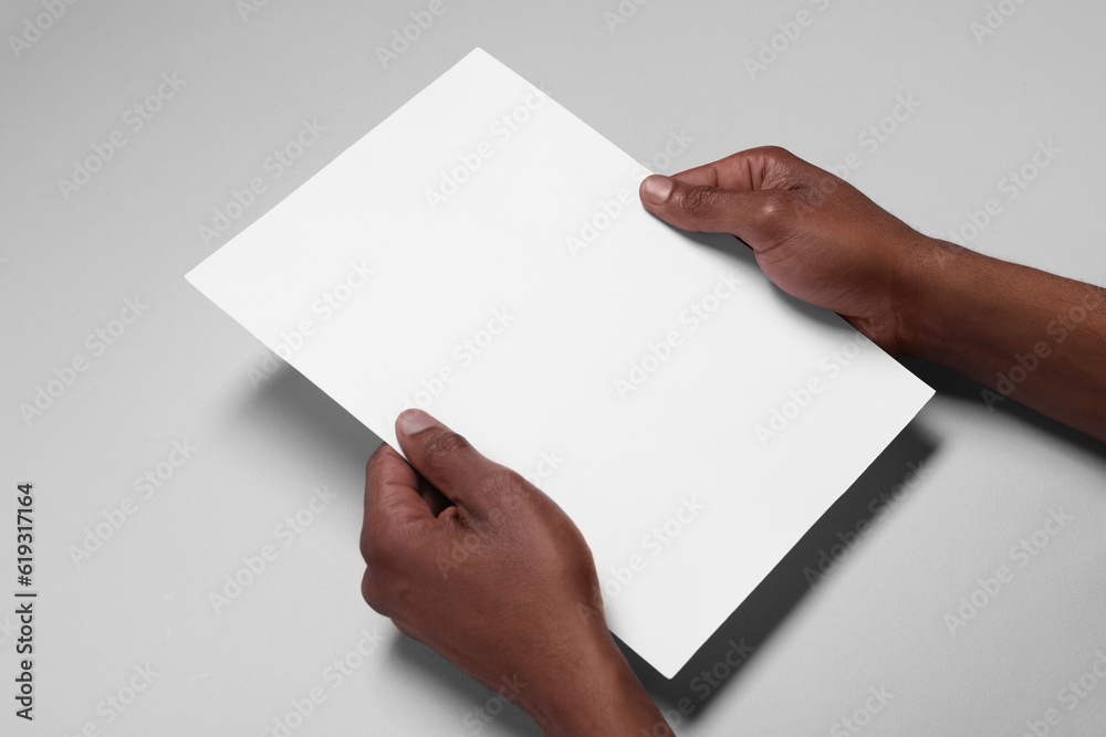 African American man holding sheet of paper on white background, closeup. Mockup for design African American man holding sheet of paper on white background, closeup. Mockup for design