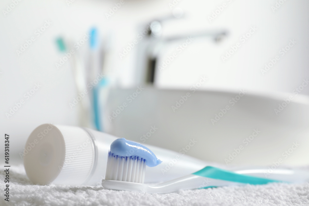 Plastic toothbrush with paste and tube on white towel in bathroom, closeup. Space for text Plastic toothbrush with paste and tube on white towel in bathroom, closeup. Space for text