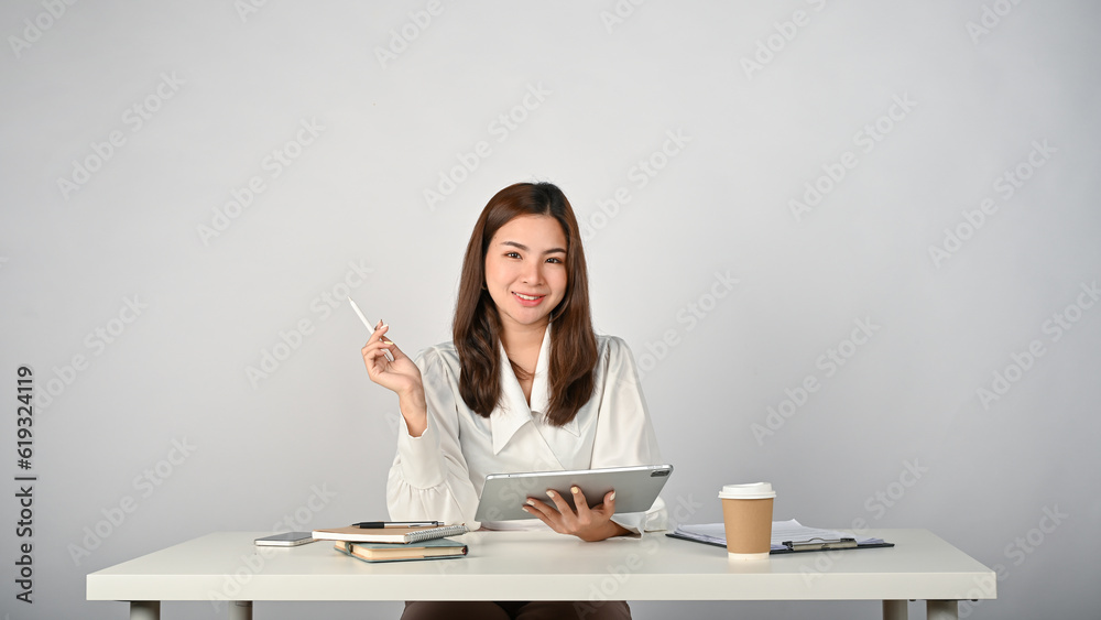 A beautiful Asian businesswoman sits at her desk with her portable digital tablet. A beautiful Asian businesswoman sits at her desk with her portable digital tablet.