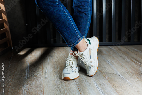 Slender female legs close-up in jeans and white sneakers made of genuine leather.